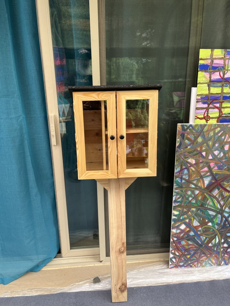 Wooden Giving Gallery cabinet during installation, with artworks visible behind it